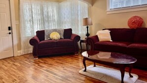 A living room with two dark red sofas, a glass coffee table, and a wooden floor. - Country Comfort near City Conveniences (Saint Paul)