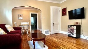 A living room with a red sofa, a wooden coffee table, a TV, and a door leading to another room. - Country Comfort near City Conveniences (Saint Paul)