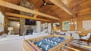 A cozy room with a foosball table, a stone fireplace, and a television mounted on the wall. - Lakeside Resort Cabin Steps to Table Rock Lake - Minutes to SDC! (Branson)