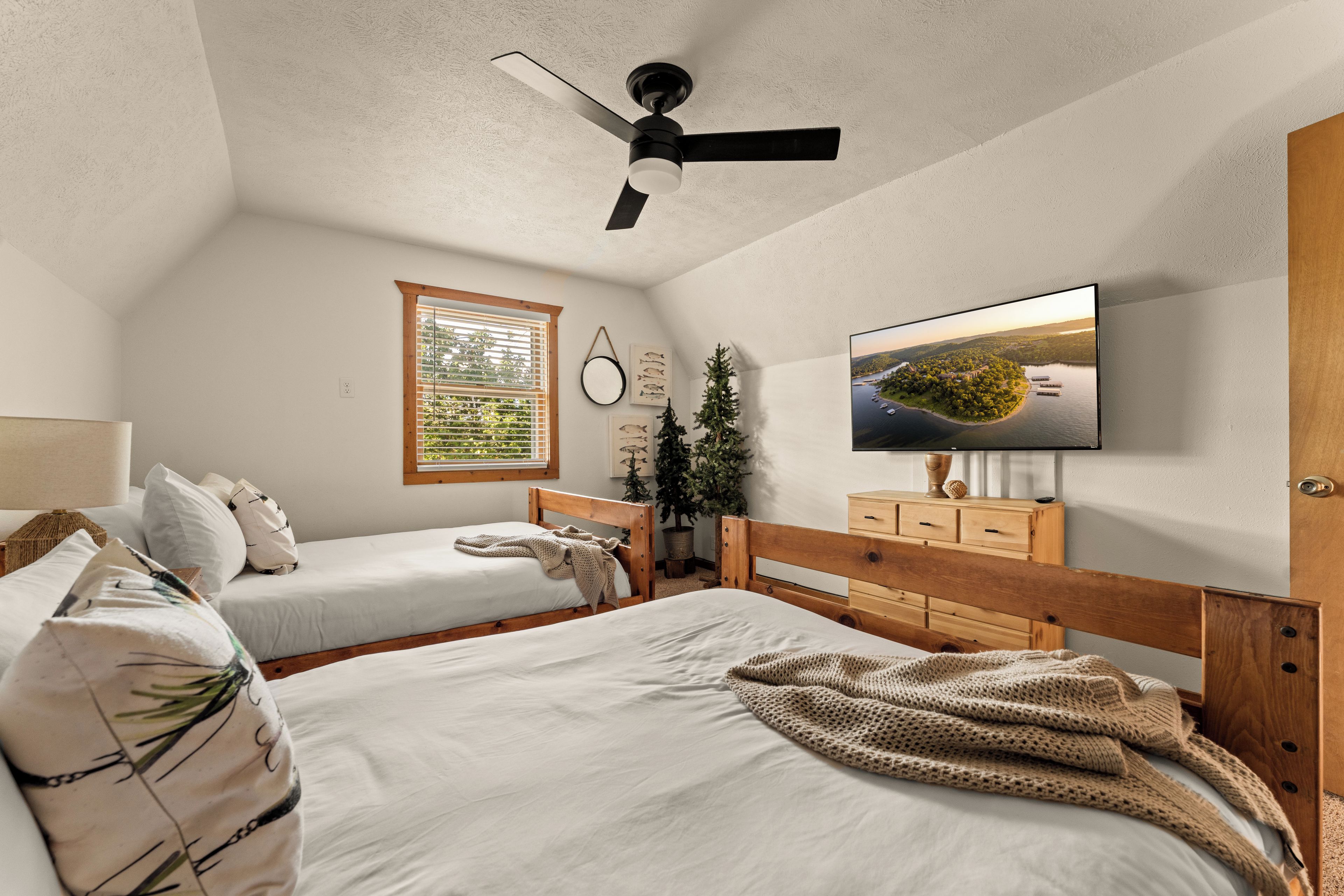 A bedroom with two beds, a ceiling fan, a television, and a window with blinds.