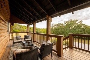 Una terraza de madera con mobiliario de mimbre y barandilla con vistas a un paisaje natural.