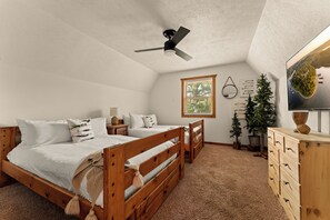 Un dormitorio con dos camas de madera, un ventilador de techo, una ventana con persianas, un árbol pequeño y un aparador.