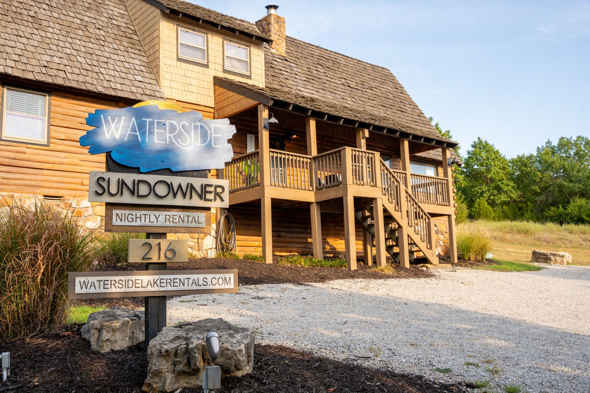 Ein Holzhaus mit Veranda, beschriftet mit 'Waterside Sundowner Nightly Rental 216'.