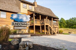 A wooden house with a porch, labeled 'Waterside Sundowner Nightly Rental 216.' - Lakeside Resort Cabin Steps to Table Rock Lake - Minutes to SDC! (Branson)