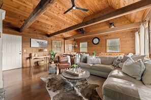 Un accogliente soggiorno con soffitto in legno, una zona divani, un tavolino da caffè e un orologio grande appeso al muro.