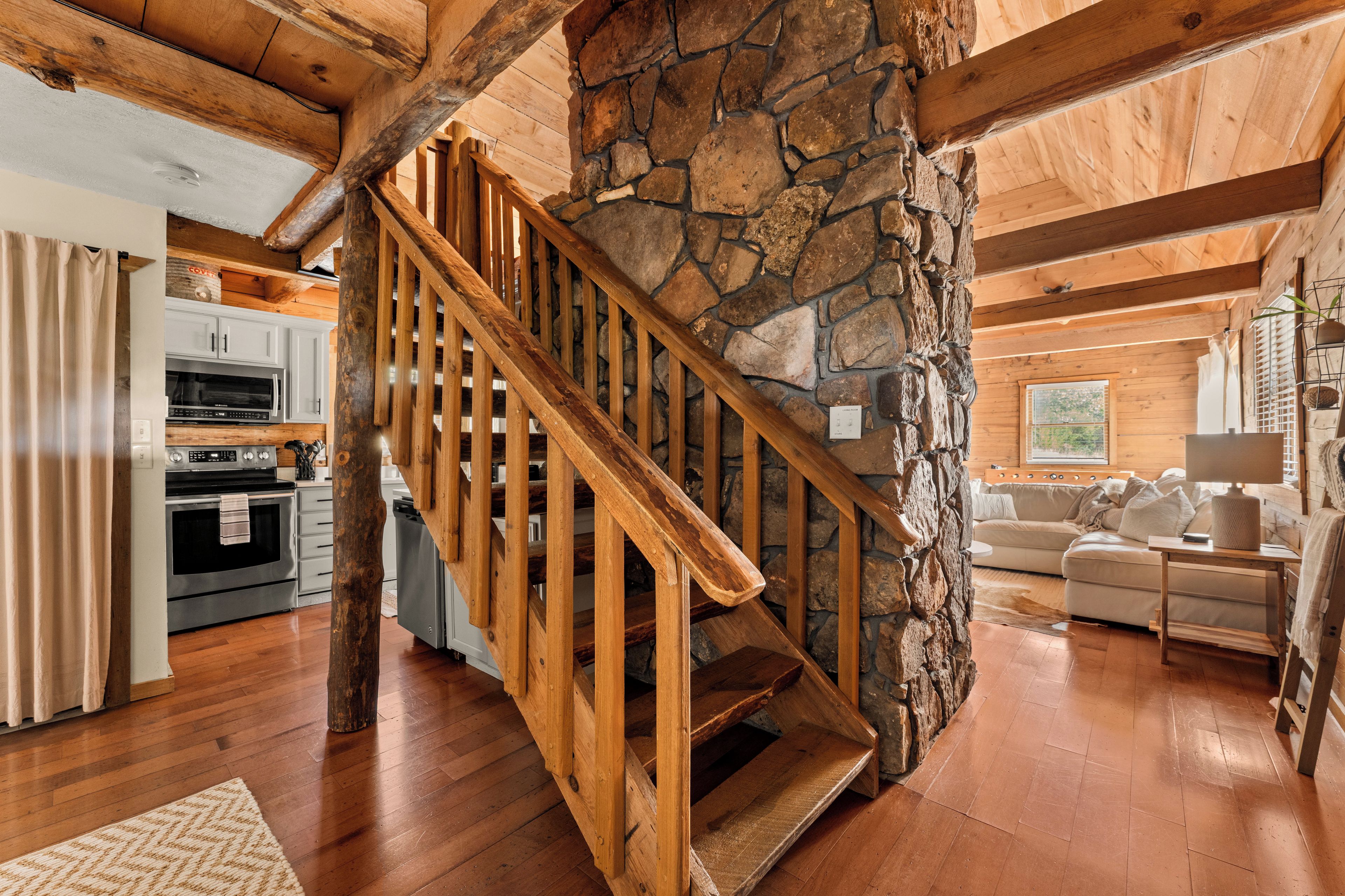 A wooden staircase with a stone wall, a kitchen with modern appliances, and a living area with a sofa.