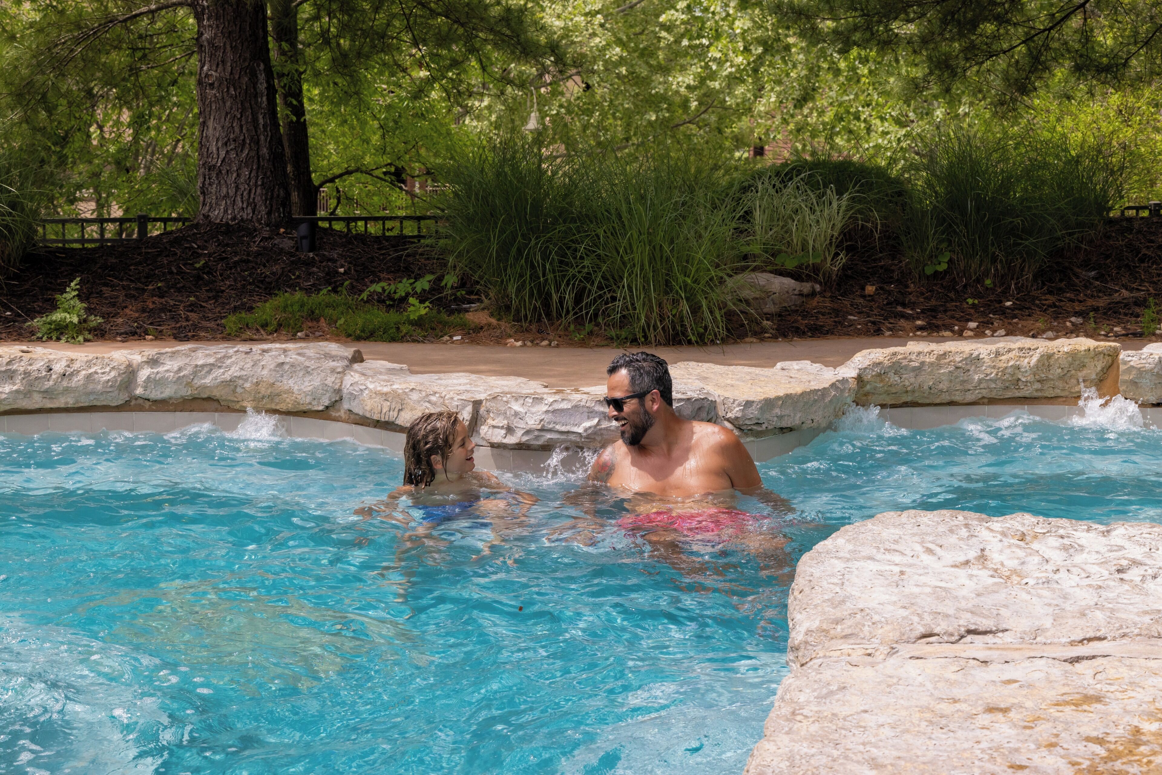 Una piscina de agua azul cristalina, rodeada de vegetación natural y muros de piedra.