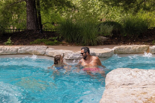 Una piscina con acqua cristallina blu, circondata da vegetazione naturale e muri in pietra.