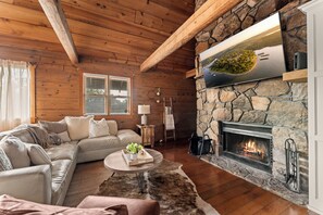 A cozy living room with a stone fireplace, wooden ceiling beams, and a comfortable seating area. - Lakeside Resort Cabin Steps to Table Rock Lake - Minutes to SDC! (Branson)