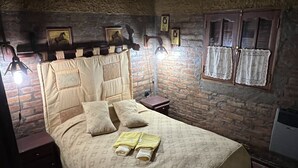 A cozy room with a bed, a nightstand, a lamp, and a brick wall.