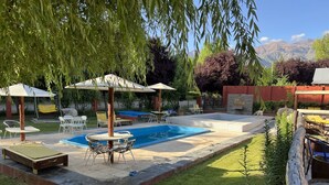 A backyard with a swimming pool, outdoor furniture, and a pergola with umbrellas.