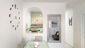 Zona pranzo moderna con tavolo in vetro, un vaso bianco e uno specchio che riflette una cucina con mobili a legno e un fornello.
