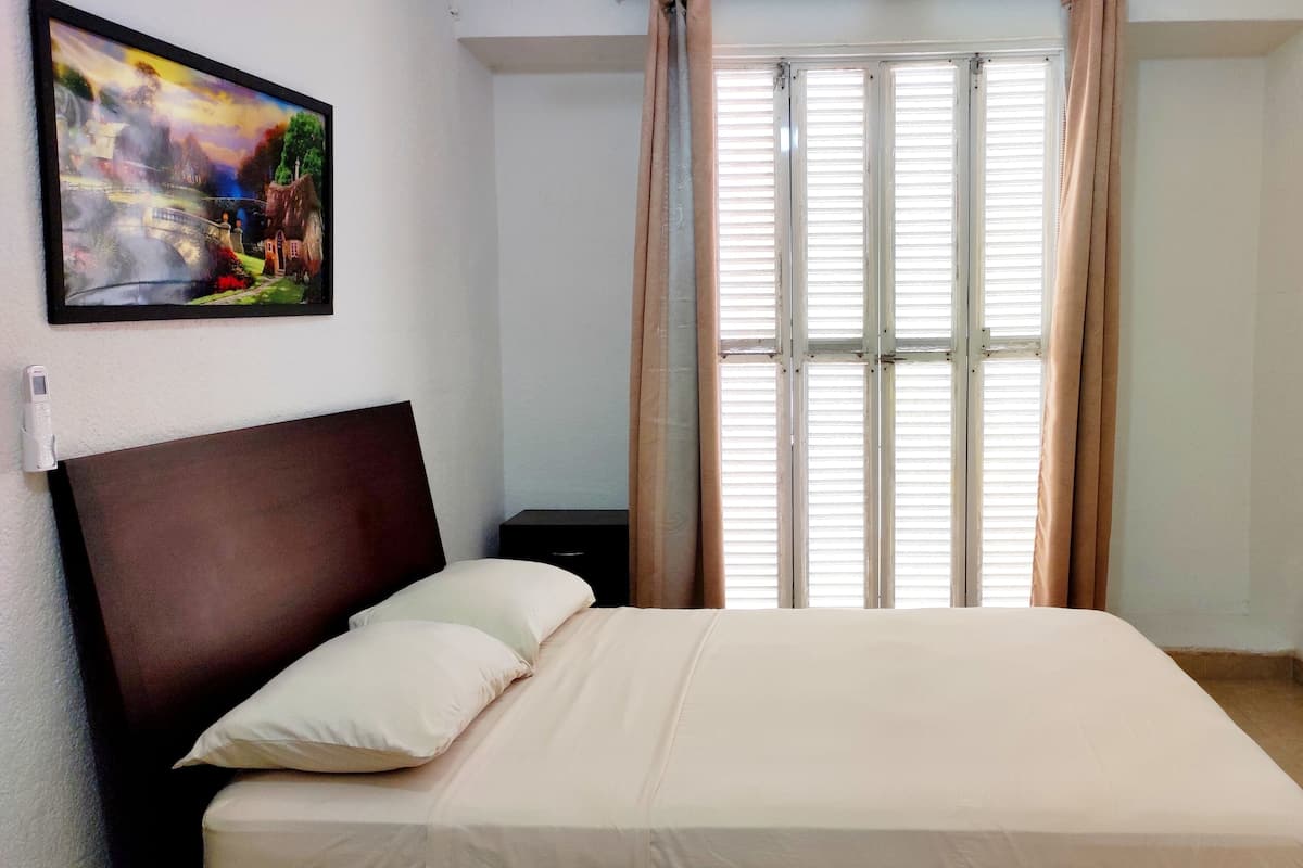 Une chambre à coucher avec un lit, une table de chevet, un tableau au mur et une fenêtre avec des rideaux.