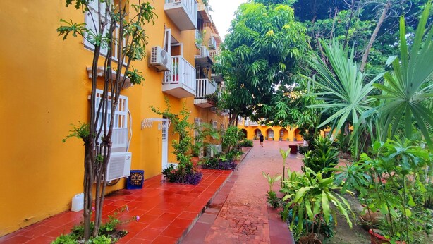 Un cortile con edifici gialli, pavimento in tegole rosse e diverse piante.