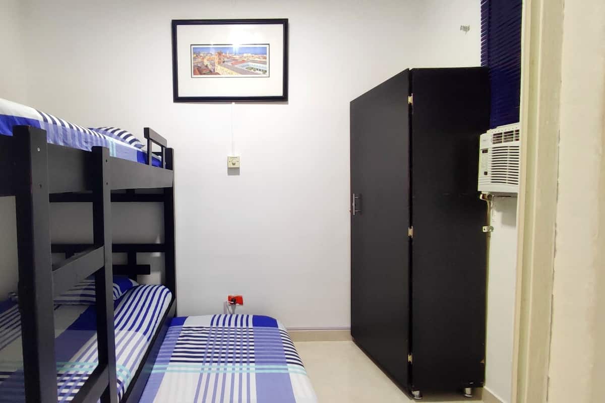 Une petite pièce étroite avec des lits superposés et une armoire noire.