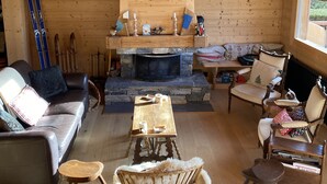 Interior acogedor de una cabaña con chimenea de piedra, muebles de madera y esquíes apoyados en la pared.
