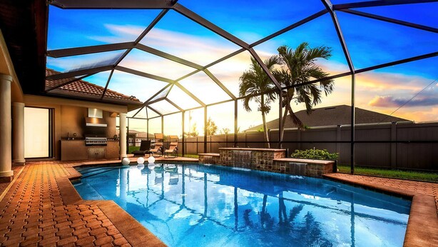 An indoor swimming pool with a clear view of the sky, a covered patio area, and a barbecue setup.