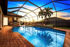 An indoor swimming pool with a clear view of the sky, a covered patio area, and a barbecue setup.