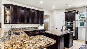 A kitchen with dark wood cabinets, granite countertops, stainless steel appliances, and a large island.