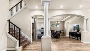 A spacious foyer with a wooden staircase, a dining area with a chandelier, and a view of the kitchen through an open archway.