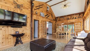 Ein gemütliches Blockhaus-Interieur mit großem Fernseher, Holzwänden, einer Essecke und einer Couch.