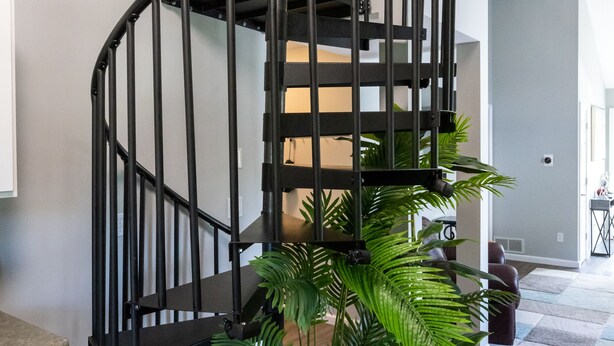 Eine moderne Wendeltreppe mit schwarzer Metallreling, umgeben von Zimmerpflanzen und einem Holzdetail.