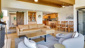 Un vaste espace de vie comprenant un canapé d’angle, une table basse et un coin repas avec des chaises en bois, ainsi qu’une cuisine en arrière-plan.