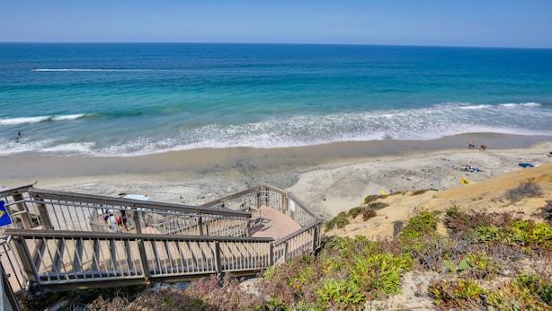 Une plage avec un escalier en bois descendant jusqu’au rivage, une plage de sable et des vagues de l’océan.