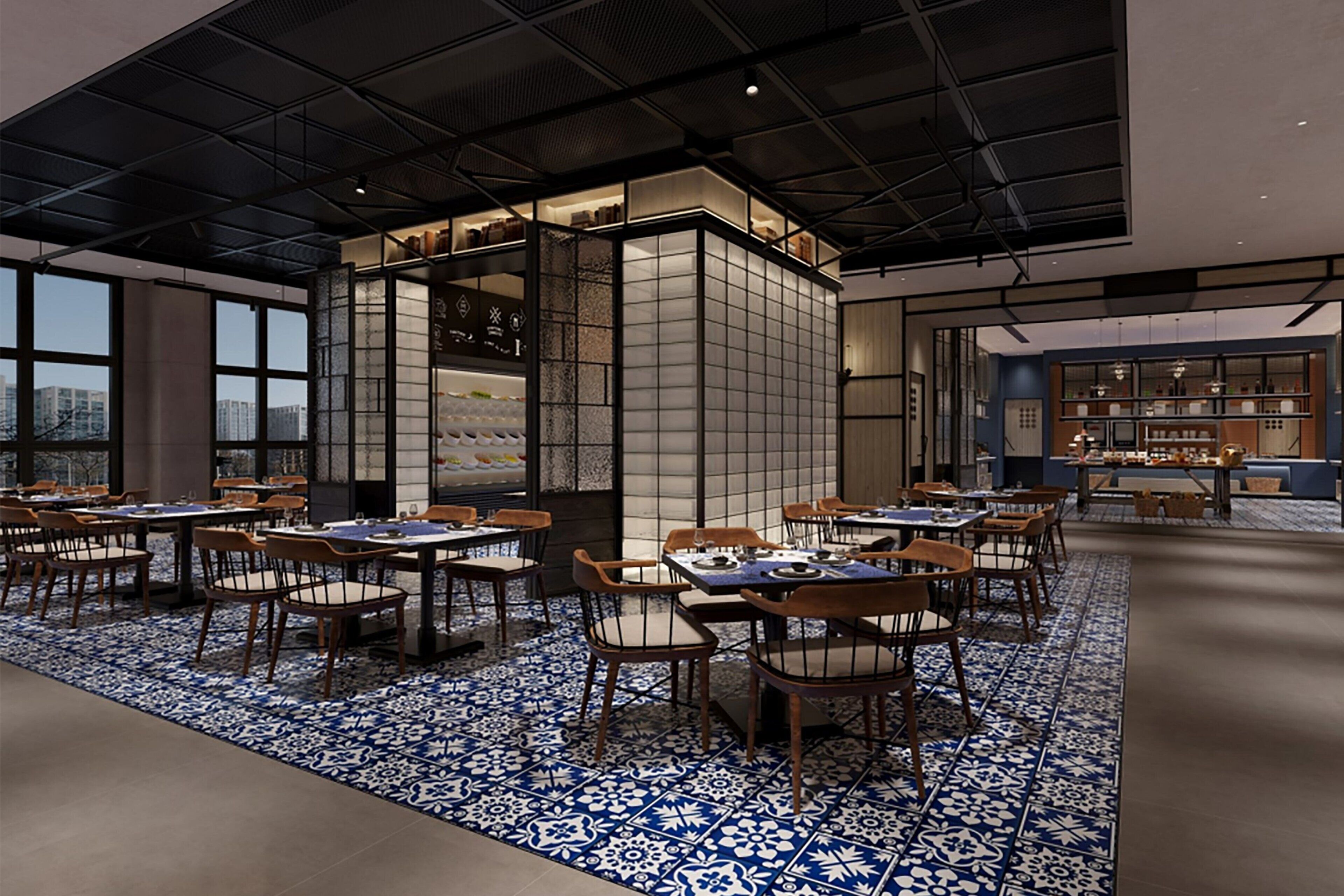 Un restaurante moderno con techo alto, ventanas amplias y suelo con estampado azul y blanco. Mesas y sillas dispuestas para comer.