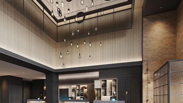 A modern lobby with a reception desk, seating area, and a high ceiling with hanging lights.