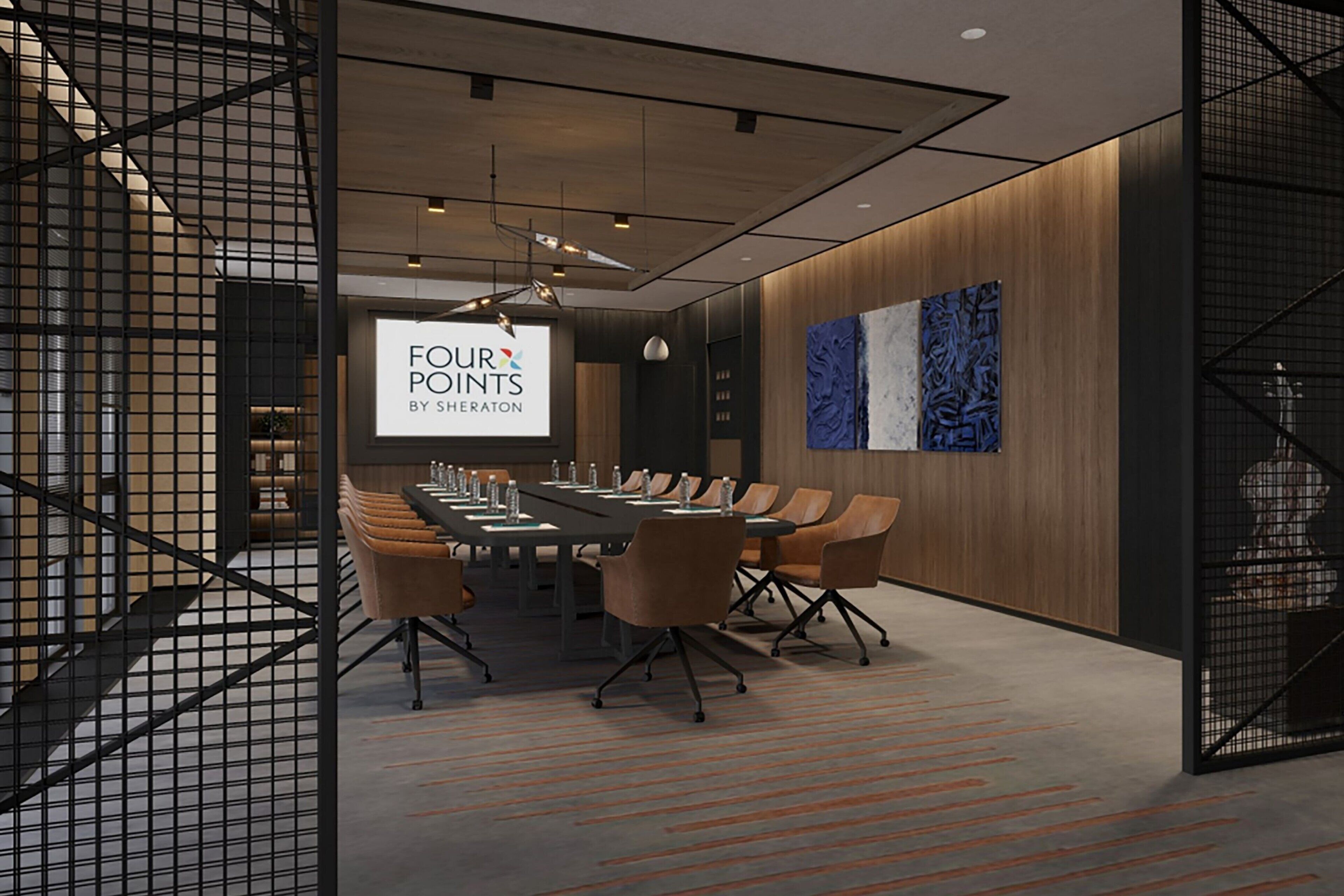 A conference room with a long table, chairs, and a screen displaying 'FOUR POINTS BY SHERATON'.