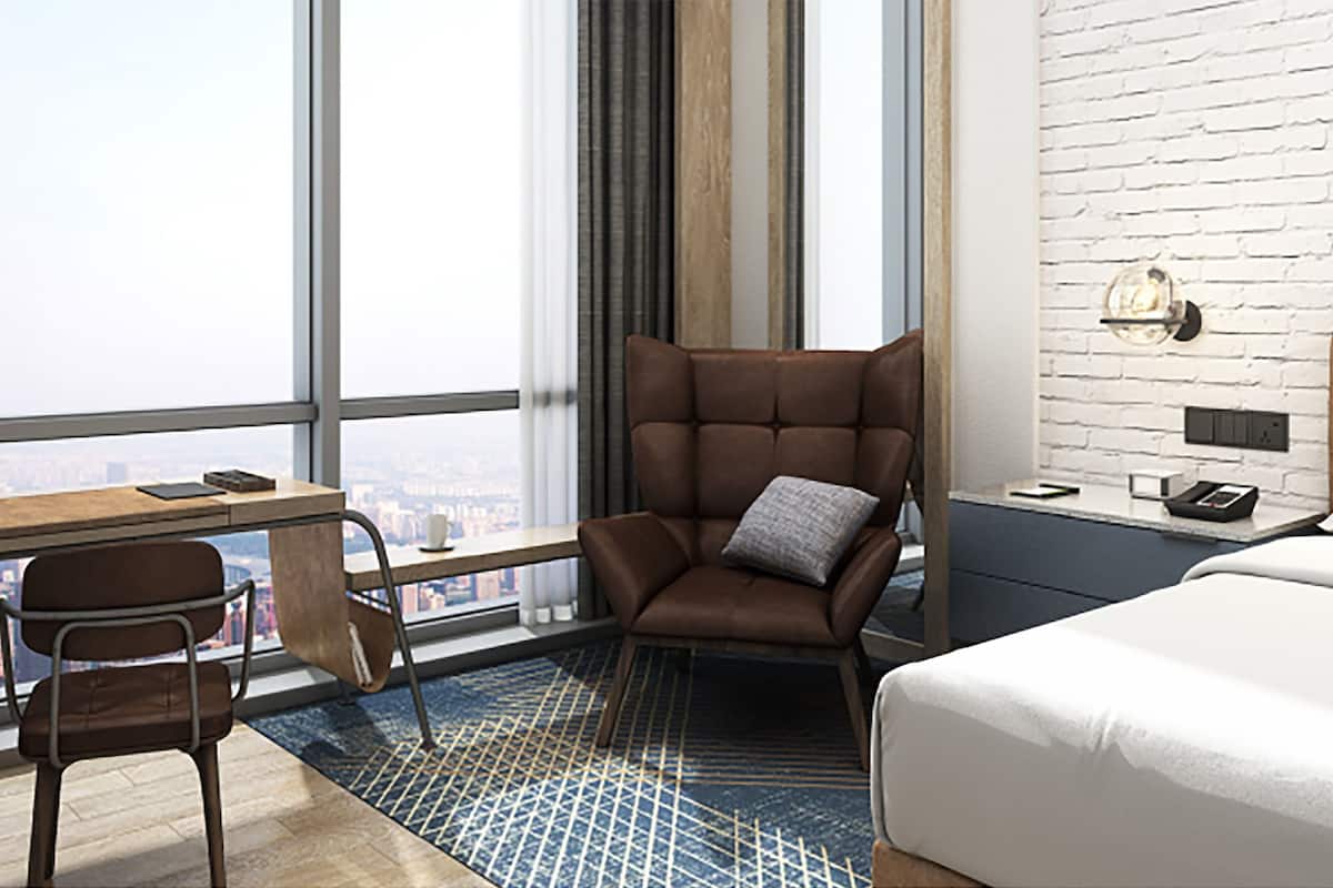 A modern hotel room with a large window, a desk with a chair, a bed, and a brick-patterned wall.