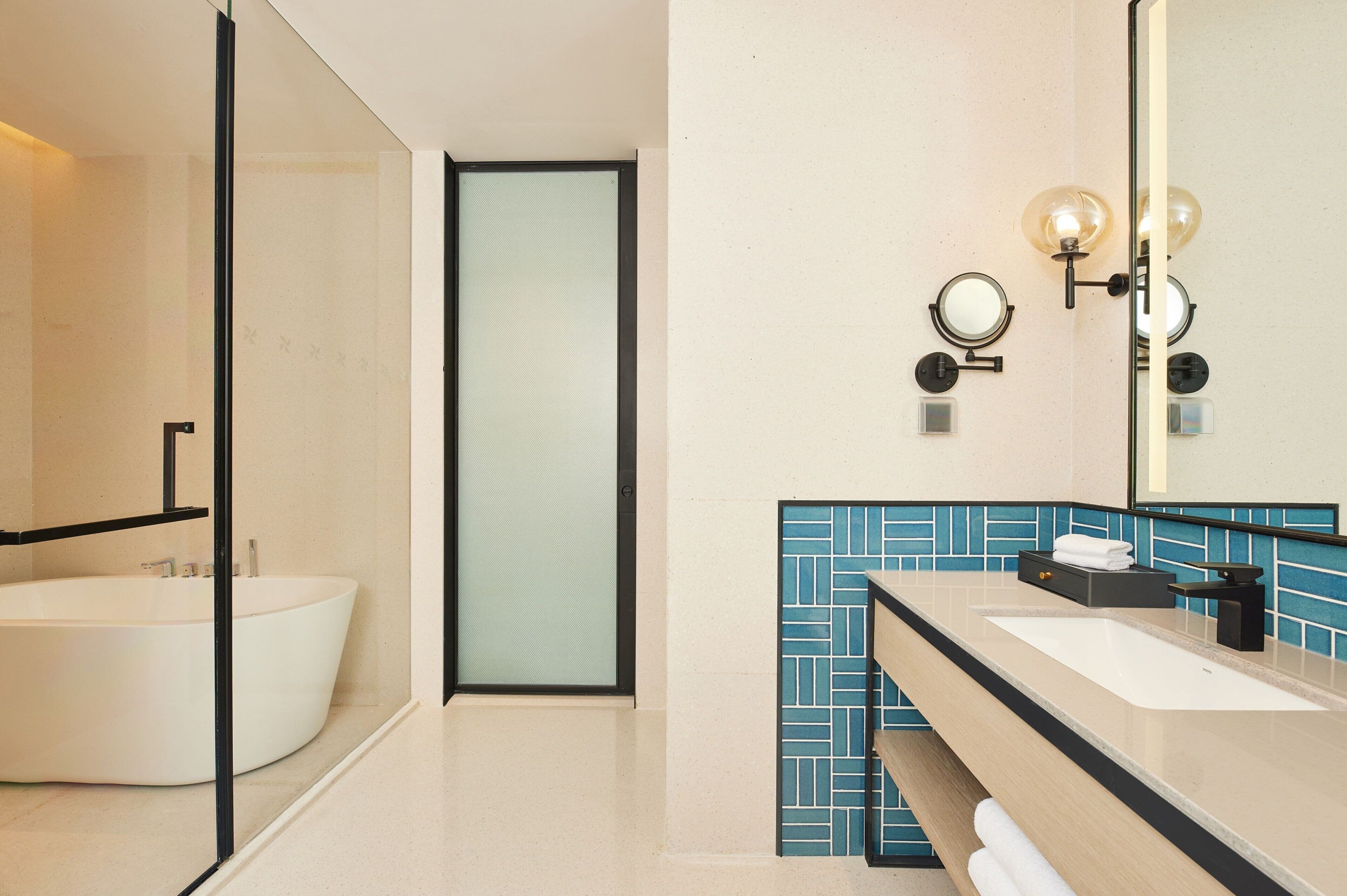 Un baño moderno con una bañera independiente, un espejo grande y un tocador con lavabo y perchero para toallas.