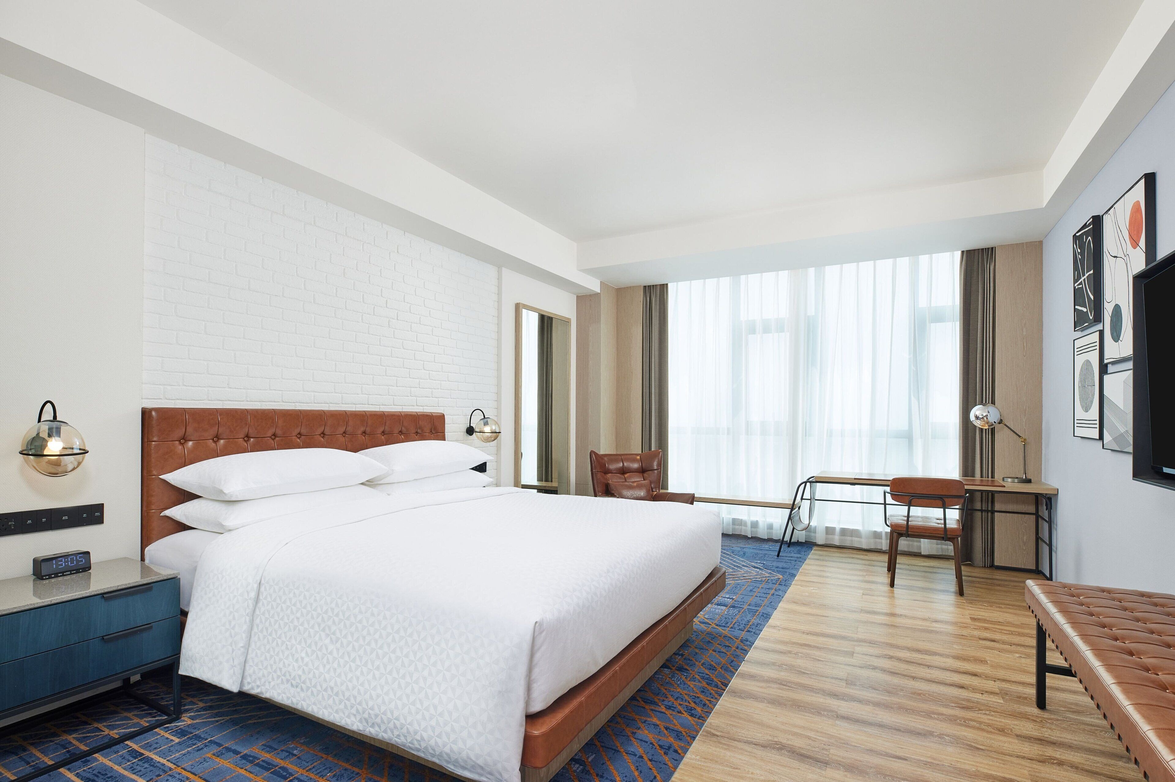 A hotel room with a large bed, a desk, a chair, and a TV on the wall.