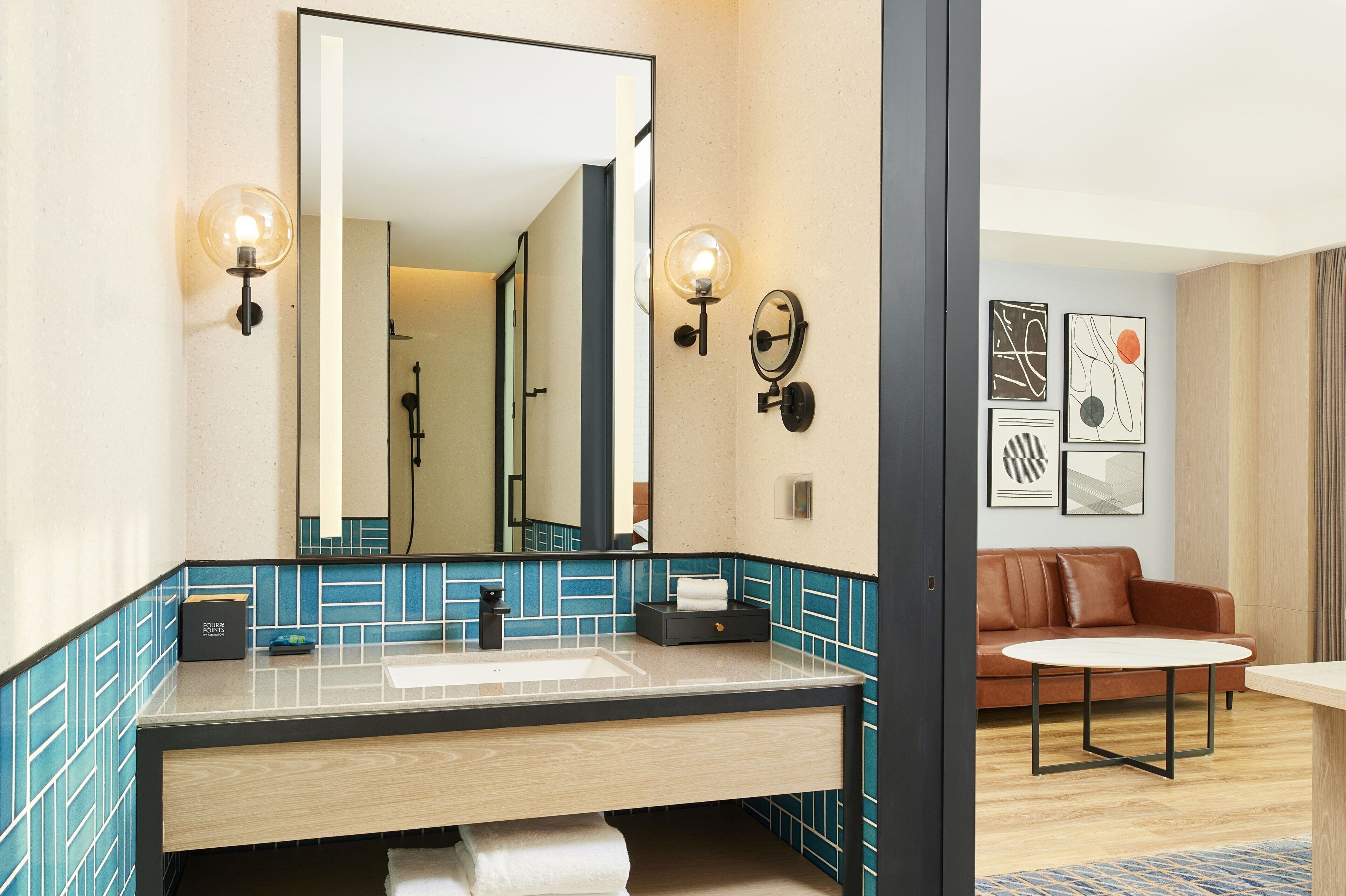 Un baño moderno con un espejo grande, dos apliques, un lavamanos y un perchero para toallas.