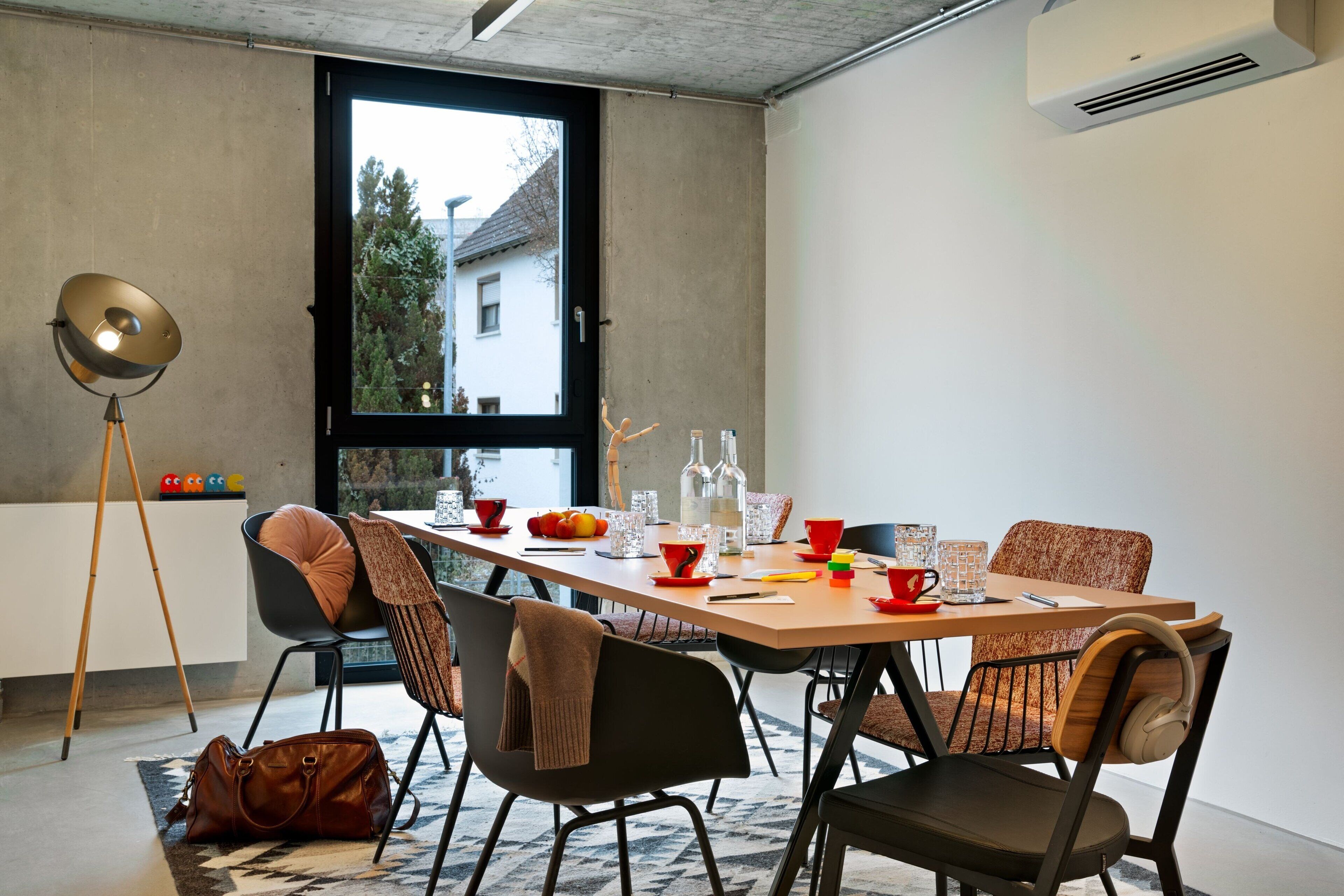 Uma sala de jantar moderna com uma mesa de madeira, cadeiras pretas e castanhas, e uma janela ampla com vista para uma casa e árvores.