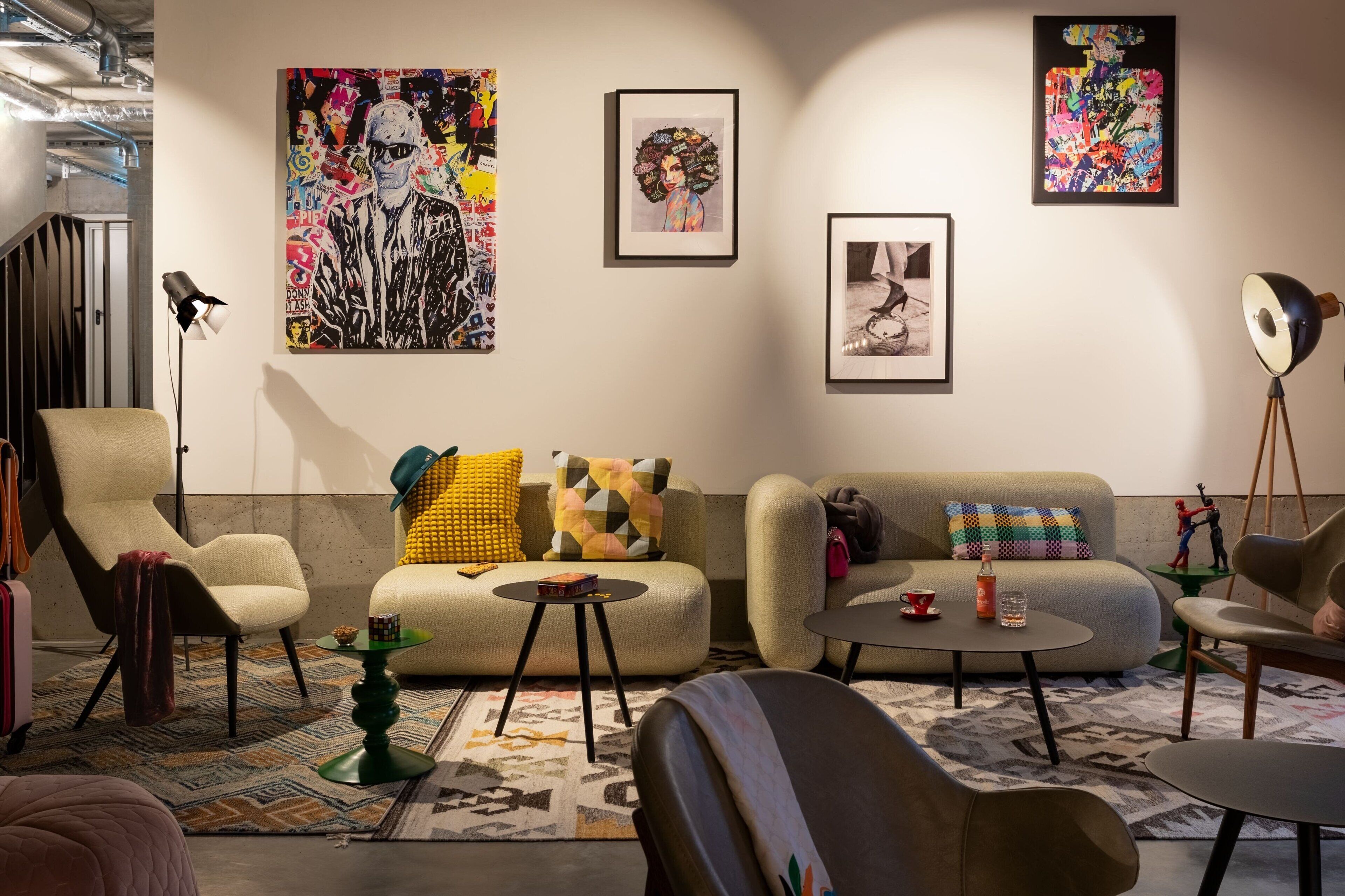 A modern living room with a sofa, armchairs, and a coffee table. There are artworks on the walls and a lamp on a tripod.
