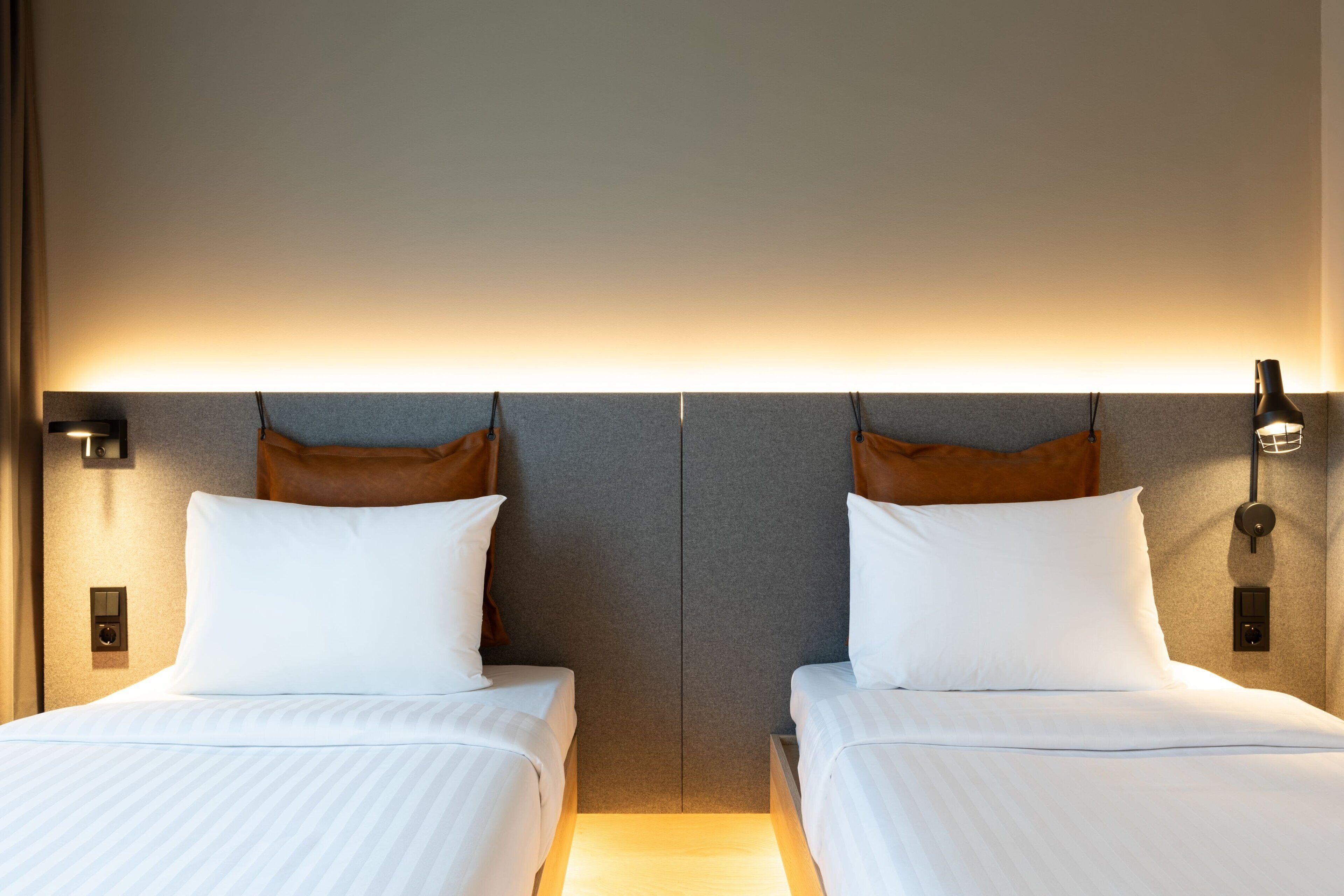 Ein Hotelzimmer mit zwei Betten, einer neutralen Farbgestaltung und modernen Leuchten.