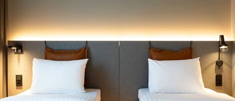 Habitación de hotel con dos camas, una paleta de colores neutros e iluminación moderna.