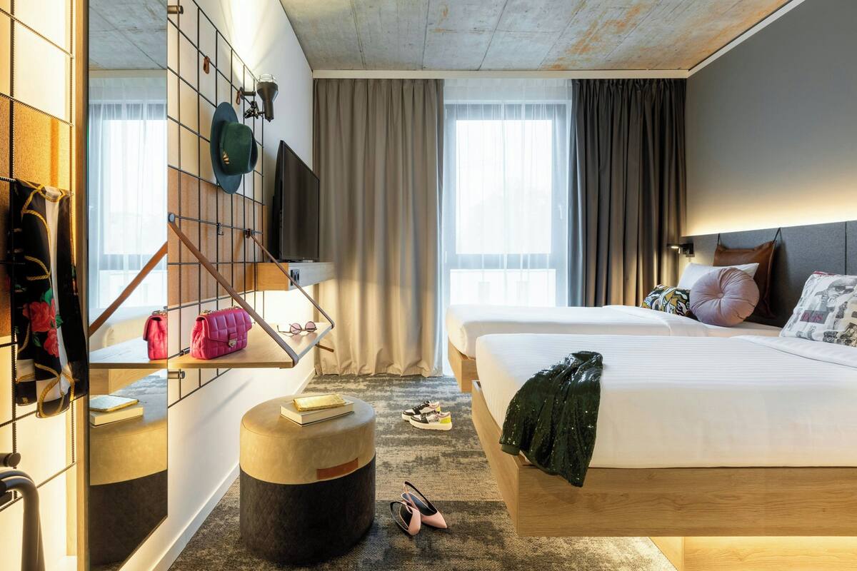 Habitació d'hotel amb un llit, zona de seients amb una cadira i taula petita, penjador i televisió penjada a la paret.