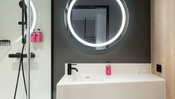 A modern bathroom with a white sink, a round mirror with a light halo, and a shower area.