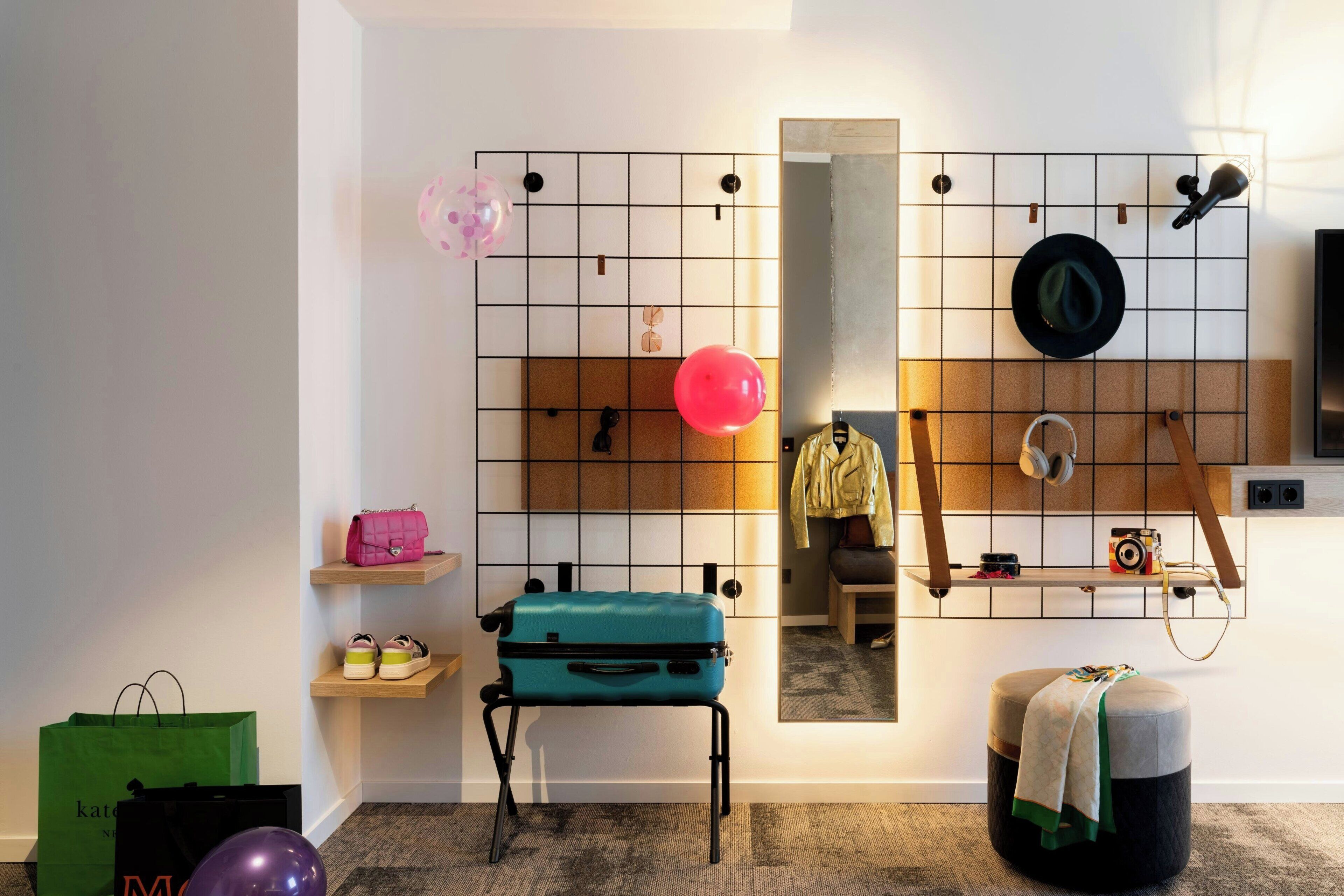 A room with a grid wall, a mirror, a suitcase, a stool, a bench, and a small table with a camera.