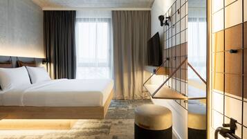 Ein modernes Hotelzimmer mit einem großen Bett, einem flachbildfernseher an einer Rasterwand und Blick ins Freie.