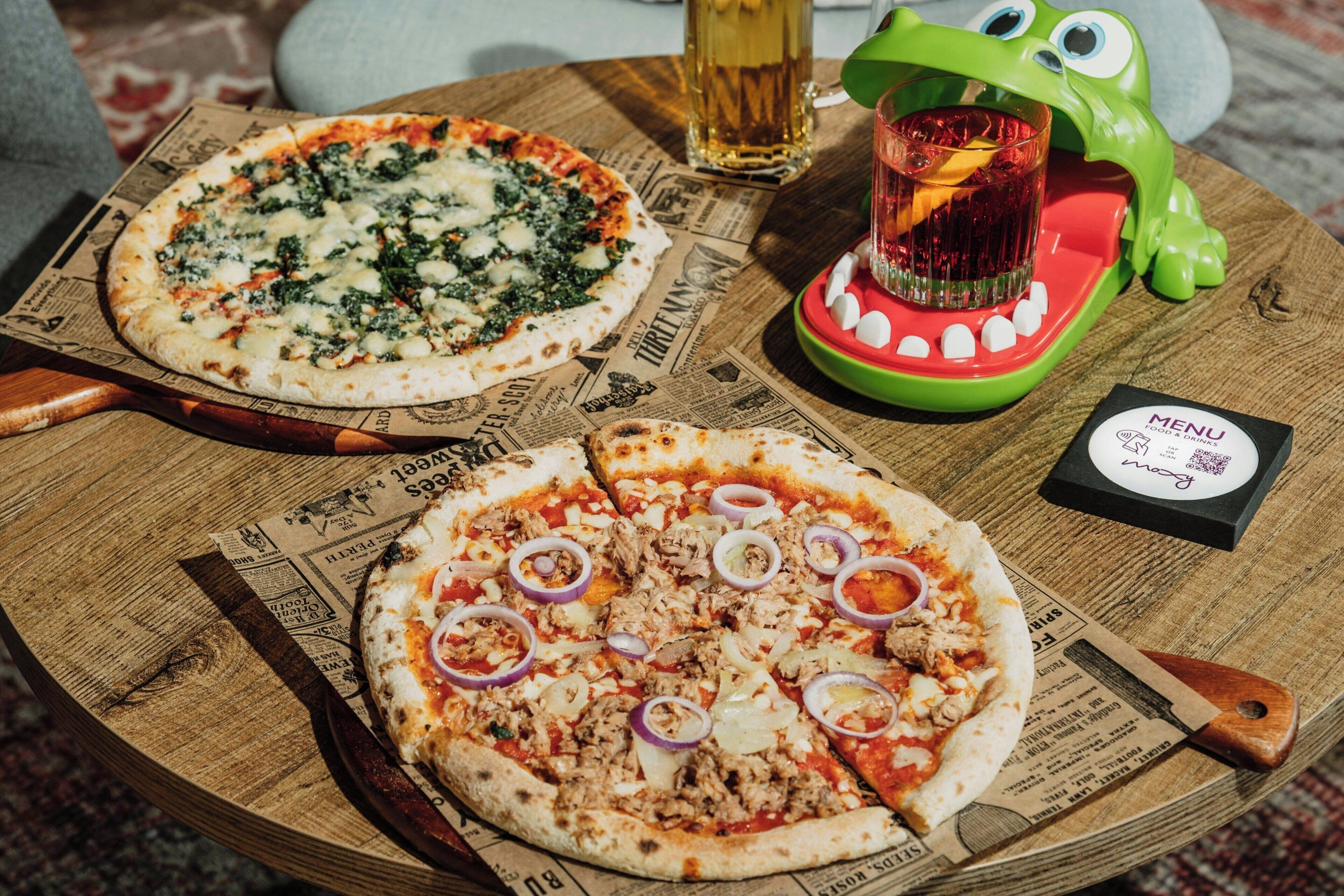 Dos pizzas sobre una tabla de madera, con un menú y una bebida en una mesa.
