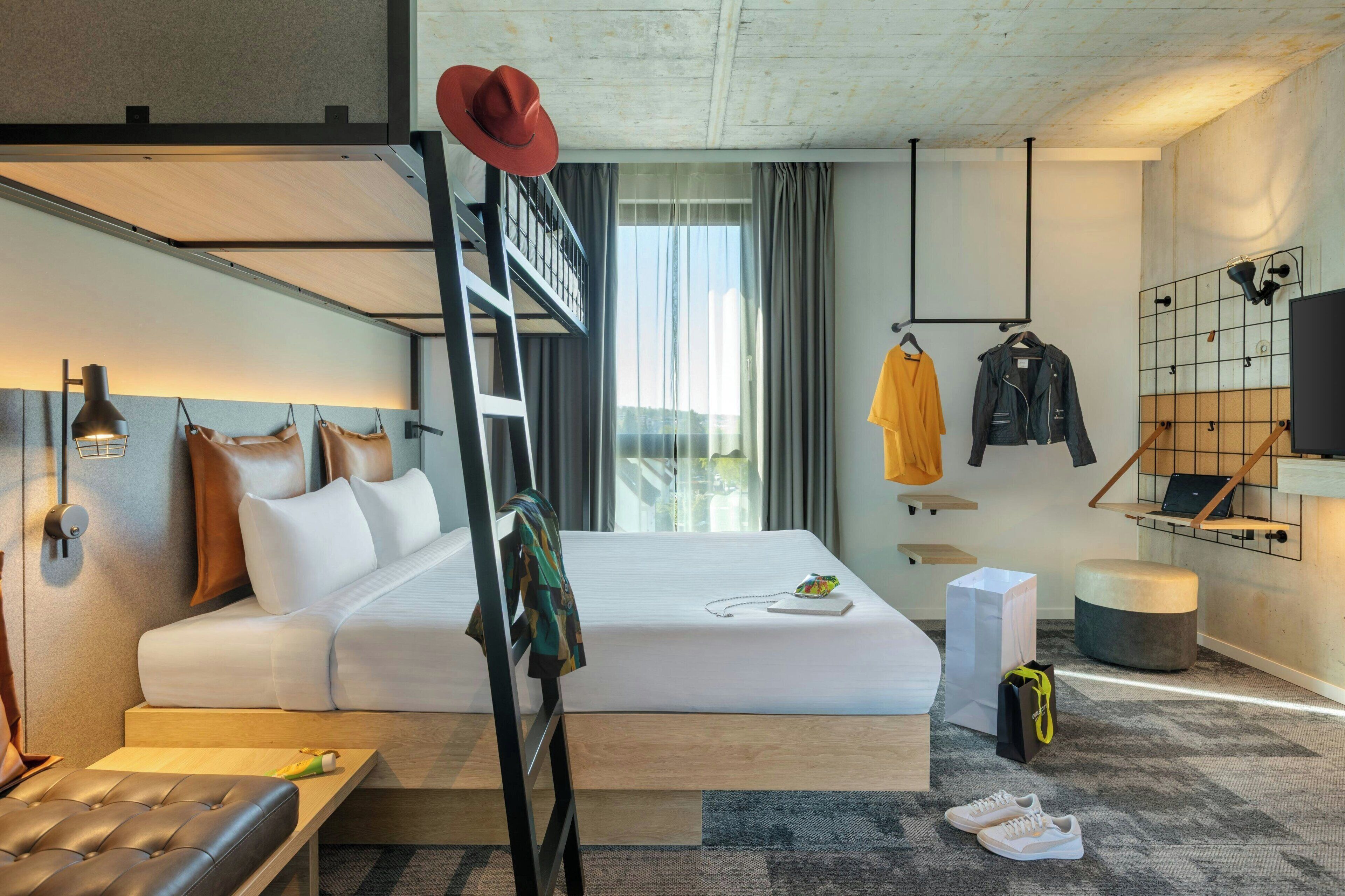 A modern hotel room with a bunk bed, a desk, a chair, a TV, and a window with curtains.
