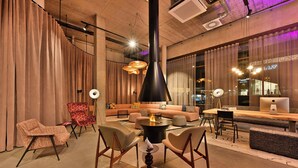 A modern lounge area with a sofa, chairs, a round table, and a fireplace. - Moxy Outletcity Metzingen (Metzingen)