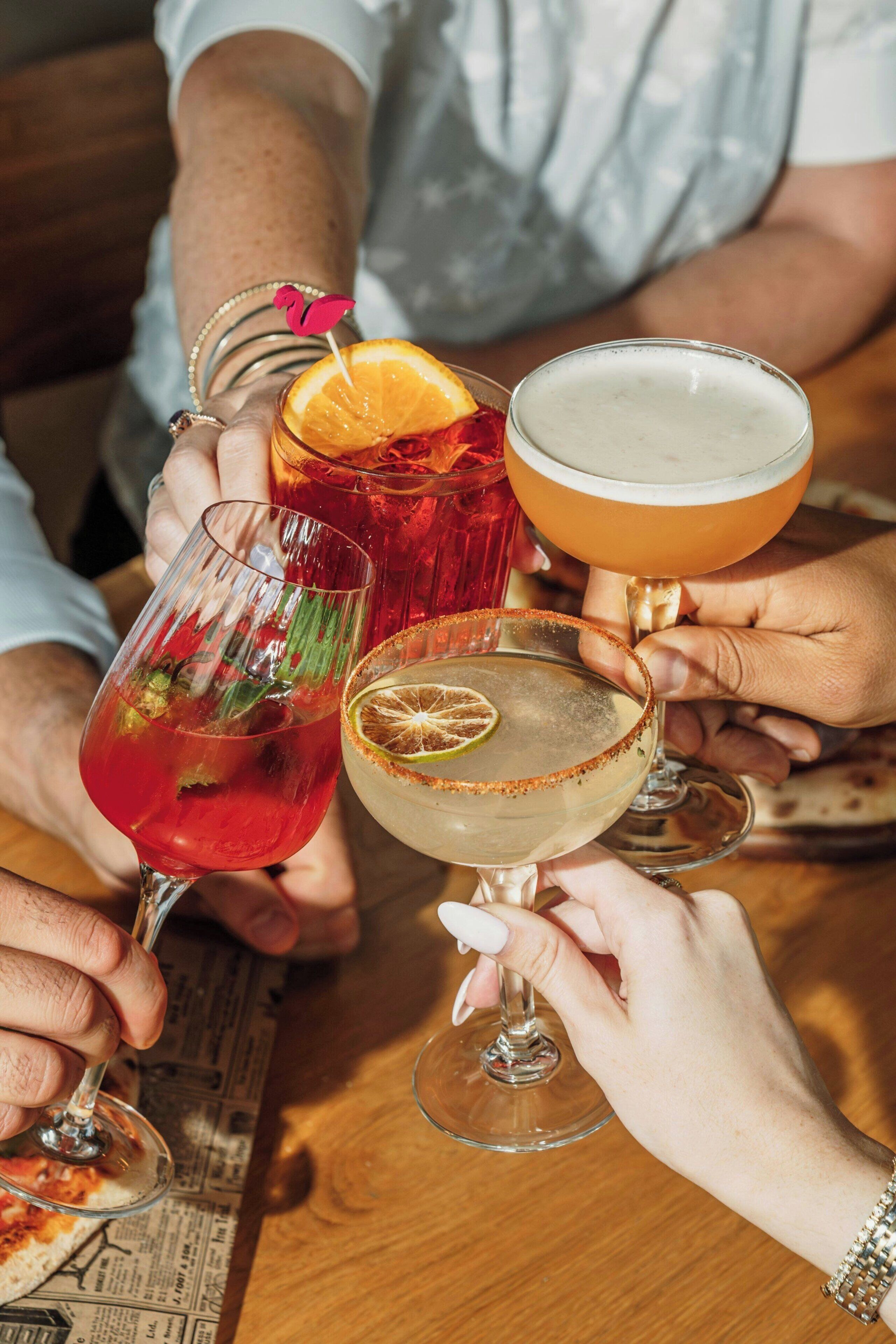 A group of people holding various types of glasses, likely containing drinks, at a table.