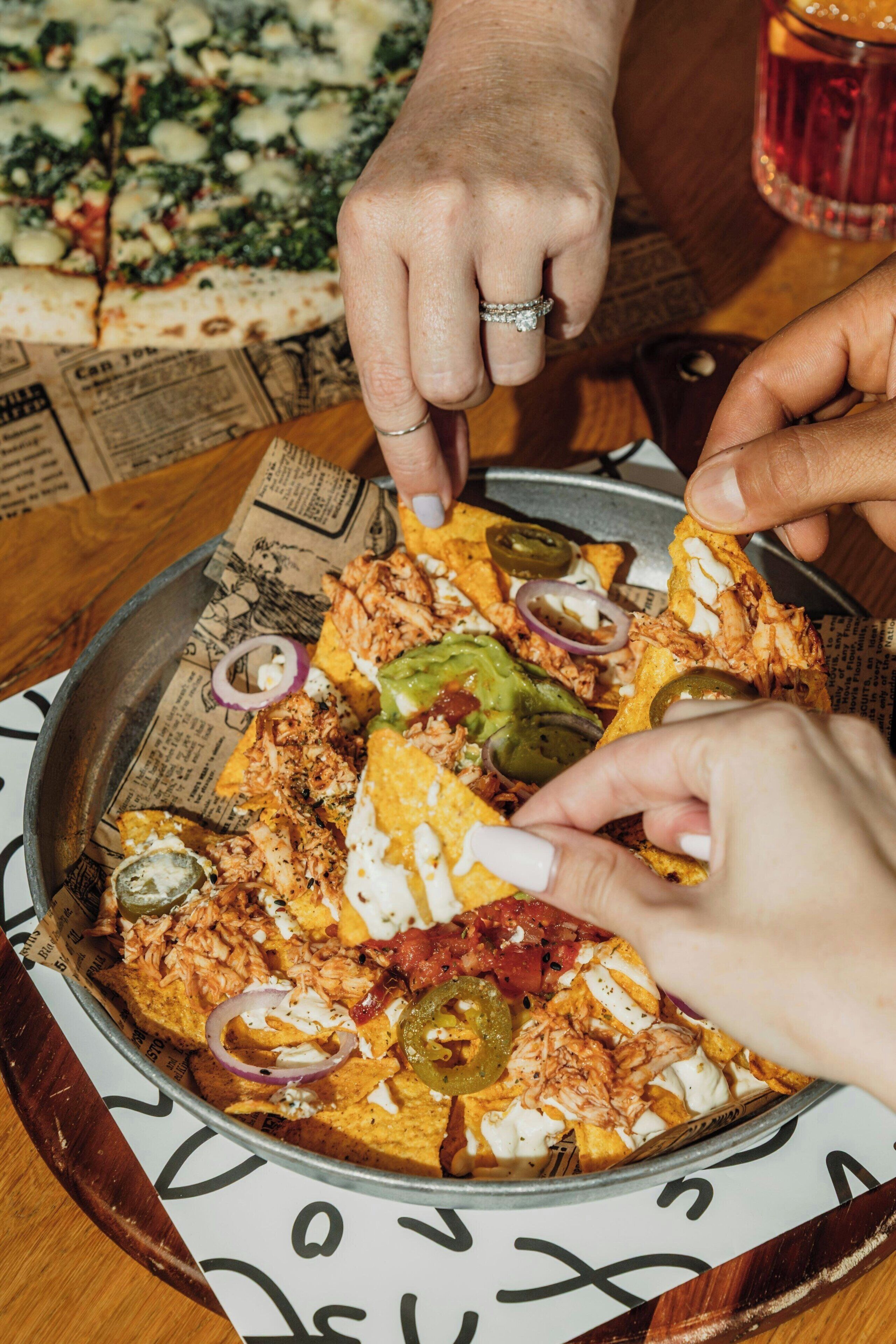 A person holding a tortilla chip with a meal.