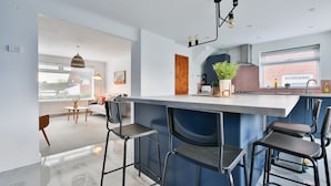 A modern kitchen with a bar area, bar stools, and a view of the living area. - Spacious 3 Bedroom House in Barry (Barry)