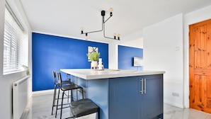 A modern kitchen with a blue accent wall, a white countertop, and bar stools. - Spacious 3 Bedroom House in Barry (Barry)